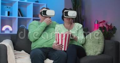 老白种人配偶一<strong>起坐</strong>在沙发上吃爆米花，在VR护目镜上看电影。 一对夫妇坐着