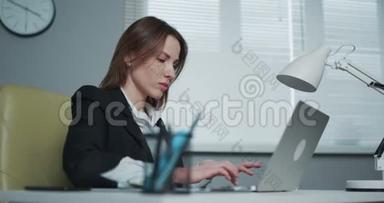 女人坐在办公桌前用笔记本电脑。 年轻的女商人正坐在办公室里写笔记本