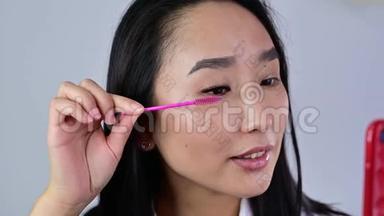 亚洲人用刷子刷她的延伸睫毛。 女人的眼皮化妆睫毛膏。 美容业。