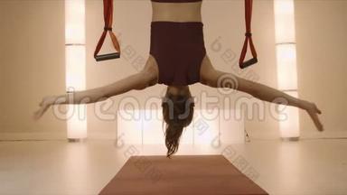 女运动员在瑜伽垫上做倒立。 女人倒吊在吊床上