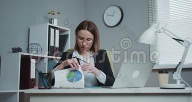 自信的年轻女商人在工作场所使用财务文件和电脑打字
