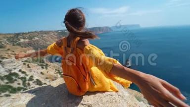 后景女旅行者穿着明亮的黄色连衣裙，背包坐在悬崖边，张开双臂迎接令人惊奇的事情
