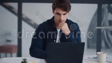 专注的商人在办公室工作笔记本电脑。 他在笔记本上读课文