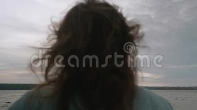 在水前的码头上，深色头发的深色头发的后视图被分散。 天空和水的背景