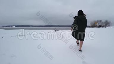 白种人深色皮肤走在地面上，池塘附近积雪覆盖。 她穿着深色外套，然后脱下，只出现在