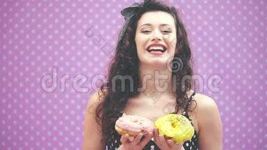 可爱的<strong>小卷发</strong>女孩站着，手里拿着两个粉红色和黄色糖霜的美味甜甜圈，开心地笑着