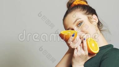 漂亮的女孩把橘子的一半水果放进耳朵里，就像耳机一样；青少年在<strong>演播室</strong>背景下玩得很开心，概念时尚