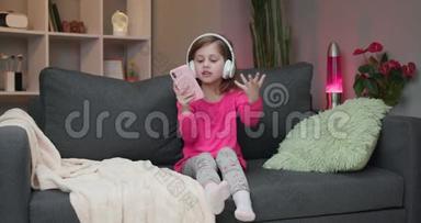 戴着耳机的小女孩在沙发上跳舞，用智能<strong>手机触</strong>摸<strong>屏</strong>幕。 现代<strong>科技</strong>和快乐