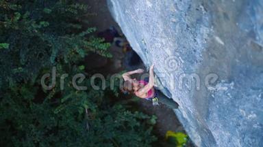 俯视女子攀岩者在艰难的运动路线上攀爬，攀岩者休息，粉笔手挂在悬崖上。