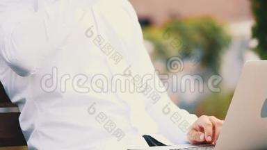 作物。 商人，穿着商业风格，坐在公园里的户外，在笔记本电脑上打字
