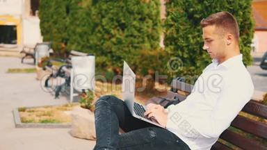 专心致志的男人，穿着商业风格，坐在公园里的户外，在笔记本电脑上打字