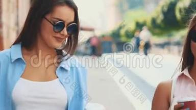 两个有魅力的年轻女人在一条带着咖啡杯的夏日街道上散步和交谈。 快关门。 复制空间。 4K