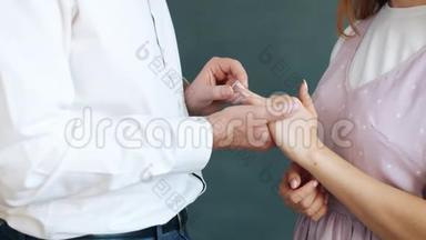 爱的男人把订婚戒指戴在女孩身上`她的手指站在<strong>灰色</strong>的背景上