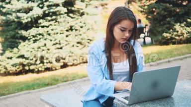 迷人的黑发女孩学生正在使用笔记本电脑在市中心，<strong>受到</strong>自然美的启发。 快关门。 复制空间