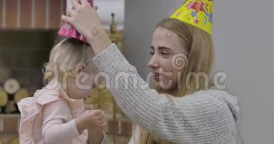 年轻的高加索女人在小女孩头上戴`派对帽。 穿着粉色上衣庆祝她第一个<strong>生日</strong>的漂亮<strong>宝宝</strong>