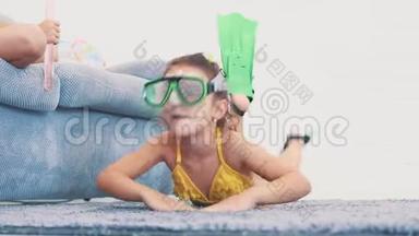 小女孩，穿着泳衣，脚蹼和护目镜模仿游泳，躺在地毯上。 复制空间。 4K.