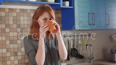 漂亮的红发女孩在家厨房喝早咖啡。 自由职业者的早晨。 享受一个困倦的早晨