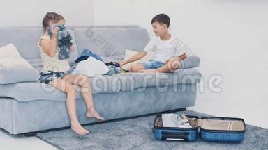 小孩子在家里把衣服扔进手提箱。 他们坐在蓝色沙发上。 特写4K..