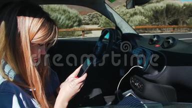 穿着牛仔夹克的漂亮金发女人坐在<strong>汽车</strong>的乘客座位上时使用智能手机。 太阳`阳光