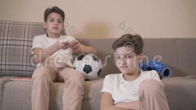 两个高加索双胞胎兄弟坐在沙发上，用遥控器切换电视频道。 类似白色T的雏鸟