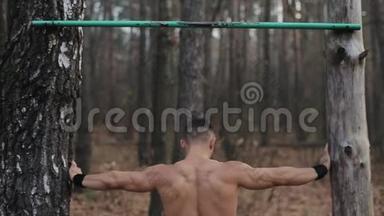 背部观看肌肉发达，英俊的白种人运动员在户外水平杆上做拉力。 健美的运动员