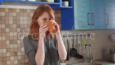 漂亮的红发女孩在家厨房喝早咖啡。 自由职业者的早晨。 享受一个困倦的早晨