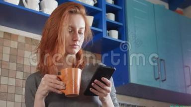 漂亮的红发女孩在家厨房喝早咖啡。 自由职业者的早晨。 使用智能<strong>手机手表</strong>