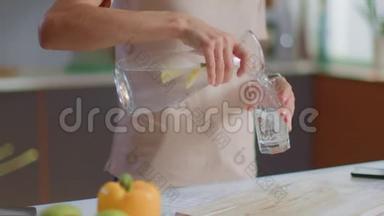 女人从家里的水壶里往玻璃杯里倒水。 女孩在厨房里喝水