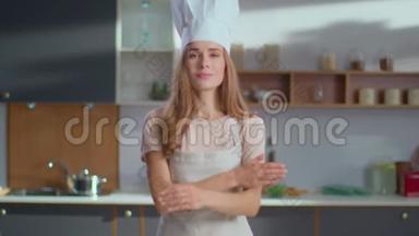 微笑的厨师站在厨房里。 女厨师戴着帽子，双手交叉着厨房