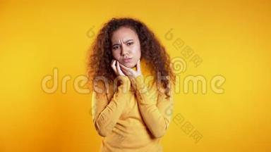 黄色摄影棚背景下牙齿疼痛的年轻美女。 牙痛