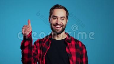 有胡子的年轻帅哥竖起大拇指，在蓝色背景上<strong>签</strong>名，对着镜头微笑。