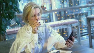 优雅时尚的金发女人坐在咖啡馆里用手机