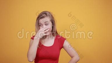 年轻的金发女孩穿着红色t恤，在橙色的背景下表现出情绪