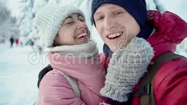 喜笑颜开的年轻夫妇在阳光明媚的冬天在雪地冬季公园散步时亲吻拥抱的特写镜头
