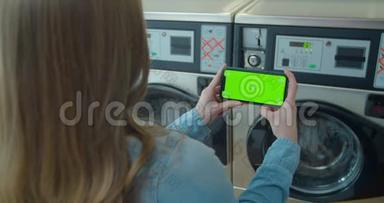 女士在<strong>洗</strong>衣店<strong>洗衣服</strong>时使用带有绿色屏幕的智能手机。 铬钥匙。 快关门。