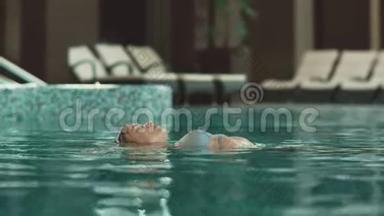 在酒店后面游泳的贴身女人。 在豪华酒店的游泳池里漂浮的女人