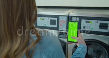 女士在洗衣店洗衣服时使用带有绿色屏幕的智能手机。 铬<strong>钥匙</strong>。 快<strong>关门</strong>。