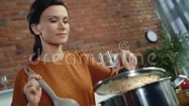 厨房里闻着热汤的女人。 家庭主妇在家厨房做饭。