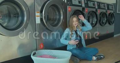 年轻女子在<strong>自助</strong>服务中坐在地板上听音乐等着洗衣服