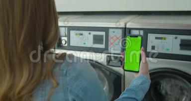 女士在洗衣店洗衣服时使用带有绿色屏幕的智能手机。 铬钥匙。 快关门。