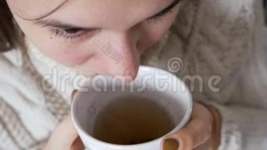 不健康的女孩拿着一杯热茶。 那个不幸的生病的年轻女子感冒了，冻僵了，对自己进行了治疗