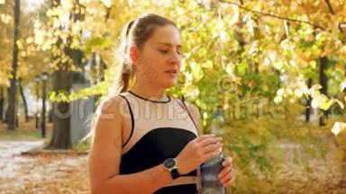4k慢动作视频：年轻微笑的女人在秋公园跑步和慢跑时，踩刹车喝水