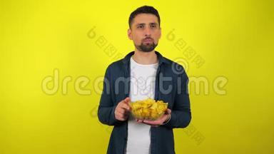 一个穿着蓝色衬衫和白色T恤的年轻人吃辛辣的薯片，用一杯水把它们熄灭