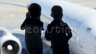 两个小男孩在机场<strong>候机</strong>楼的大窗户外等待登机的剪影片段