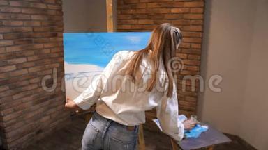 女孩学会画画。 她拿着调色板上的蓝色油漆，把它放在画布上。 4K慢慢