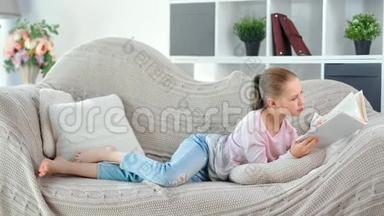 忙碌的、体贴的、年轻的<strong>女孩子</strong>在舒适的客厅里躺在沙发上看书。