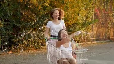 4K慢动作视频：两个笑着的女孩坐在购物车里，在大<strong>商场</strong>的停车场吹肥皂泡
