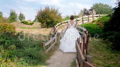 4k<strong>视频</strong>，美丽的年轻金发<strong>新娘</strong>身穿白色长裙，在长木栅栏旁的乡村散步