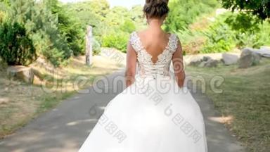 4K慢镜头<strong>视频</strong>：年轻美丽的<strong>新娘</strong>穿着白色长裙在公园的小路上走
