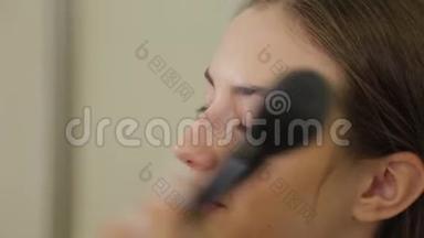 专业化妆师正在用刷子`客户的脸上涂粉。